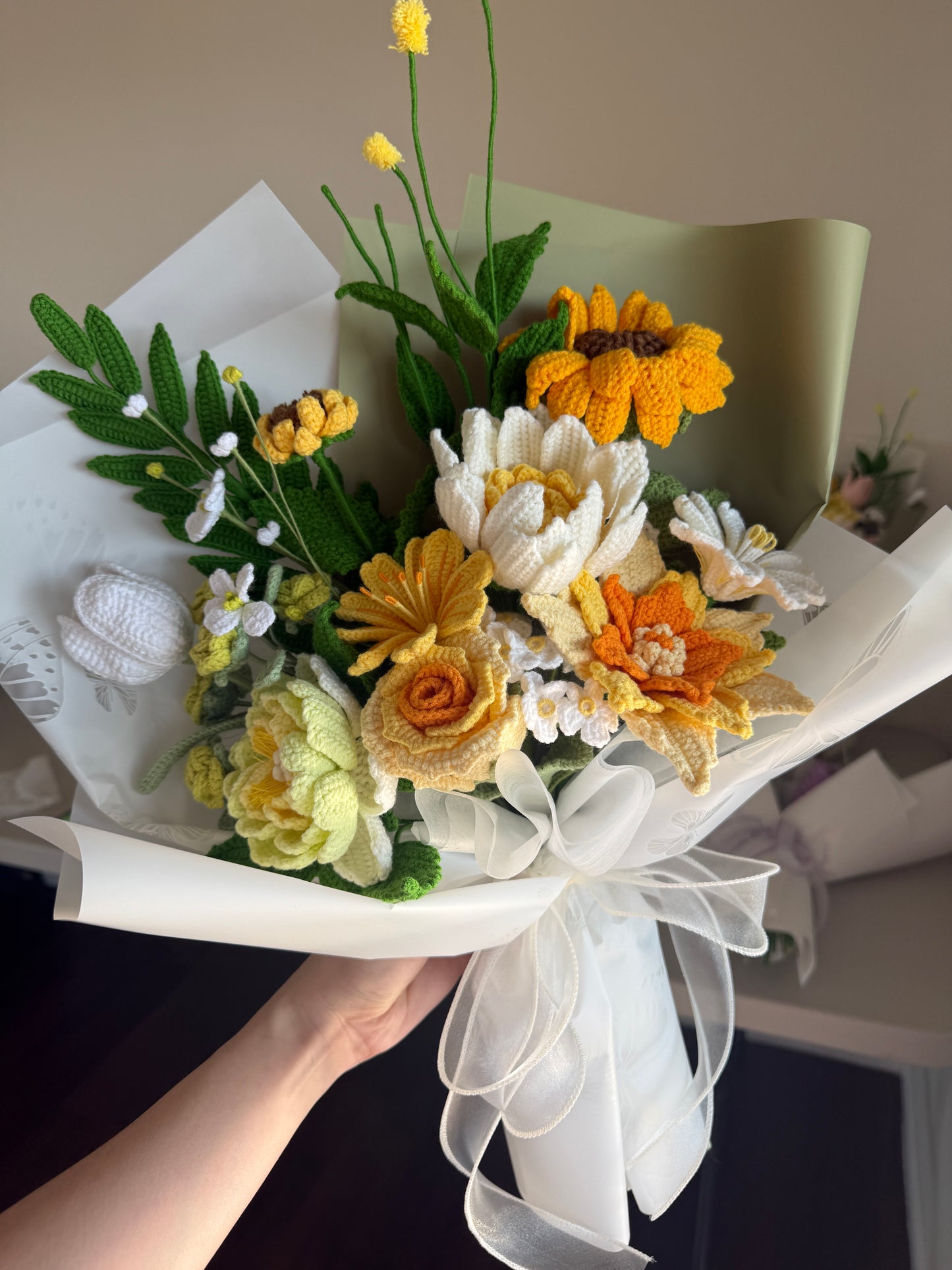 Bouquet of knitted flowers with green leaves and white ribbons on a neutral background