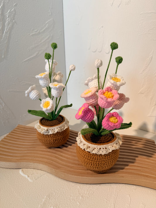 Knitted flower arrangements in brown pots on a textured surface