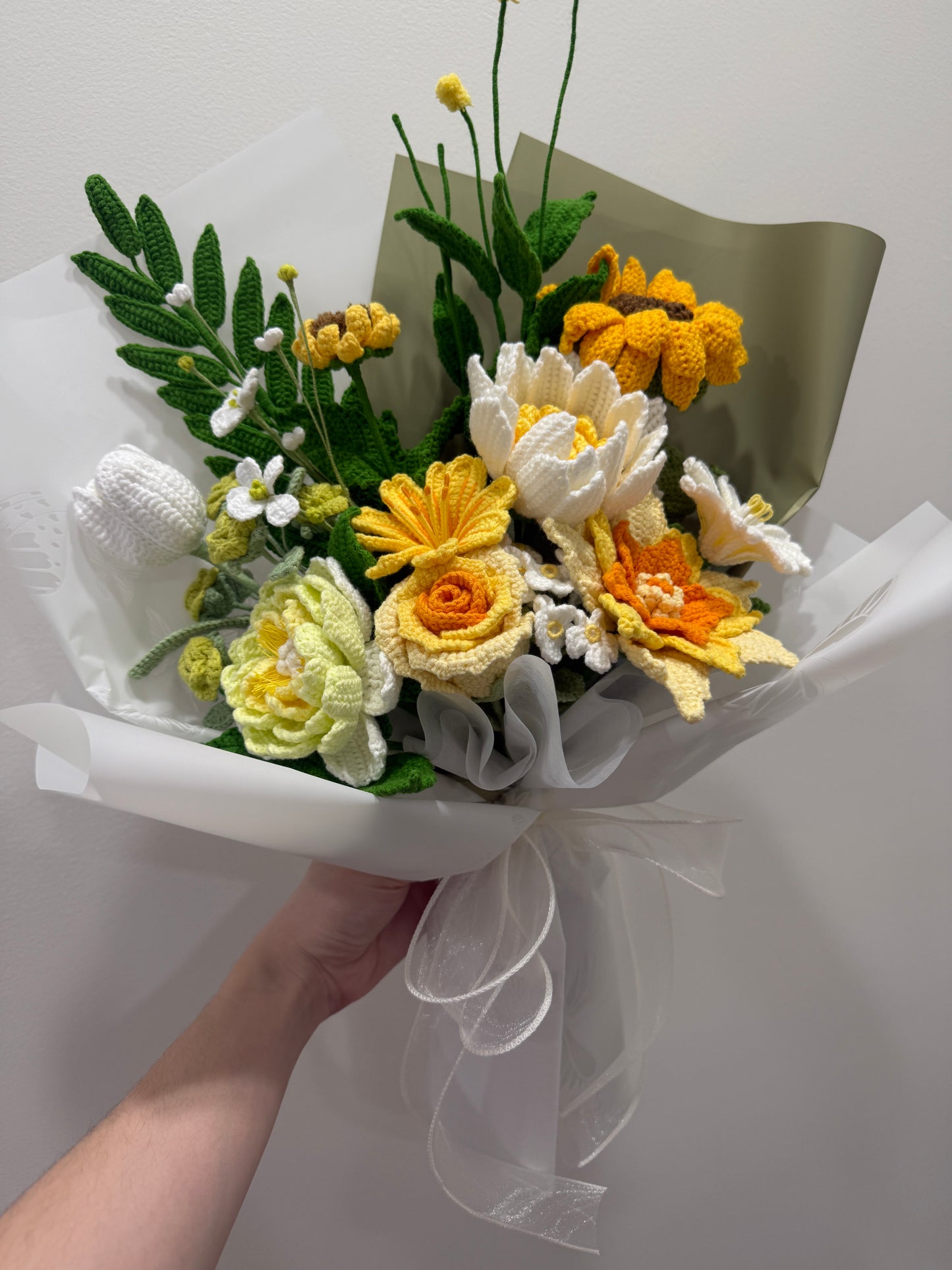 Bouquet of yellow, white, and orange flowers wrapped in paper with a hand holding it.