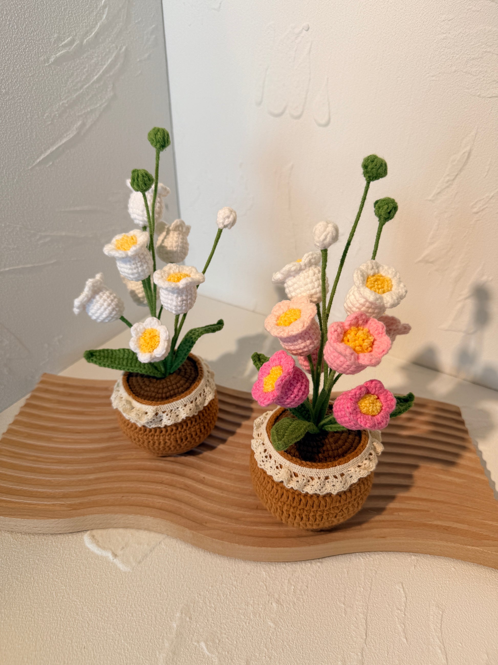 Knitted flowers in brown pots on a textured surface