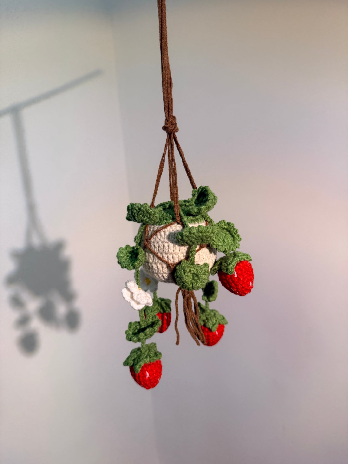 Crocheted strawberry branch with green leaves on a white background