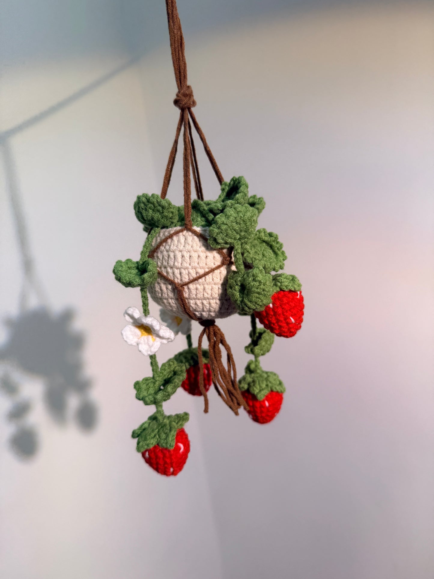 Crocheted strawberry branch with a white ball on a light background