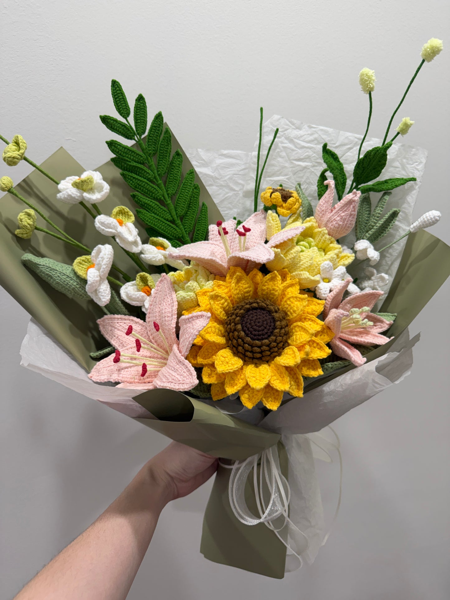 Bouquet of flowers with a sunflower held by a hand on a light gray background